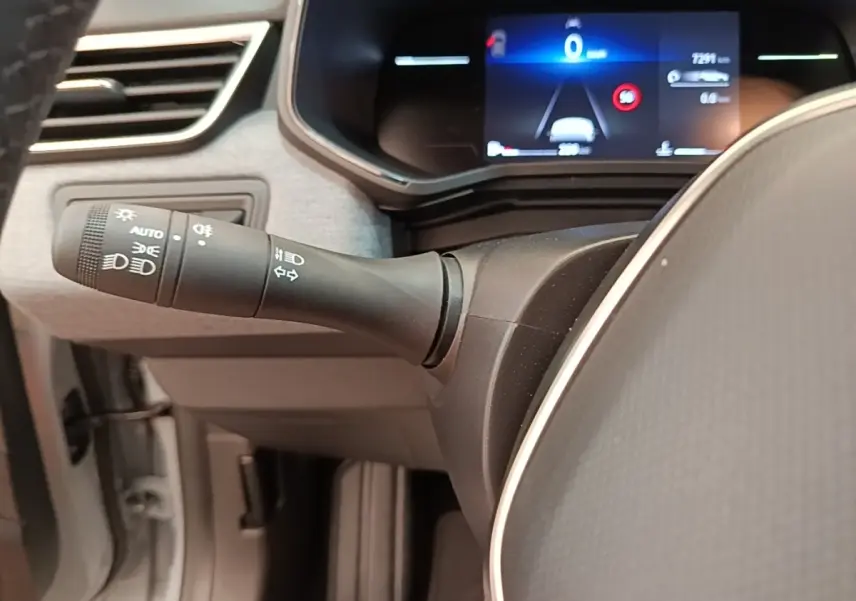 Vue rapprochée du commodo d’éclairage à gauche du volant cuir synthétique de la Renault Clio gris clair 2025.