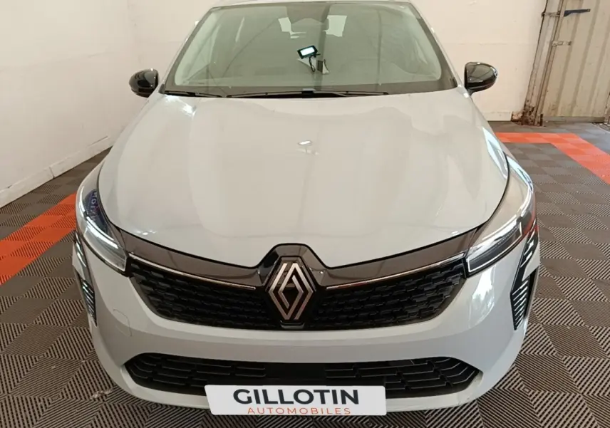 Vue avant de la Renault Clio gris clair 2025 avec calandre noire et phares LED allumés en intérieur.