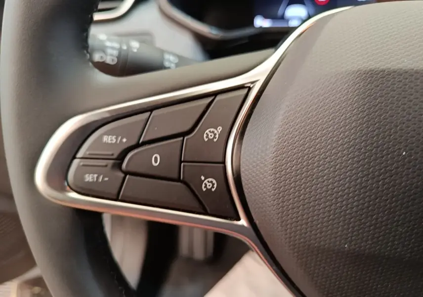 Gros plan sur les commandes du volant cuir synthétique de la Renault Clio gris clair, avec boutons de régulateur de vitesse.