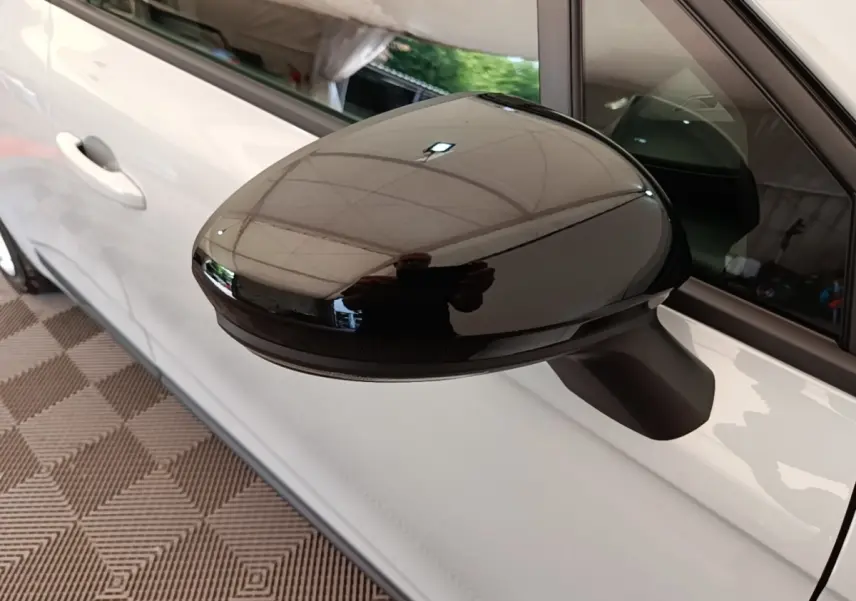 Gros plan sur le rétroviseur droit noir brillant d’une Renault Clio gris clair, vue latérale côté droit.
