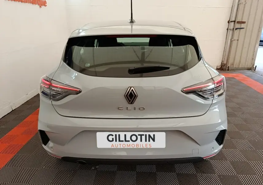 Vue arrière d'une Renault Clio gris clair 2025 avec feux LED et spoiler de toit visible en intérieur showroom.