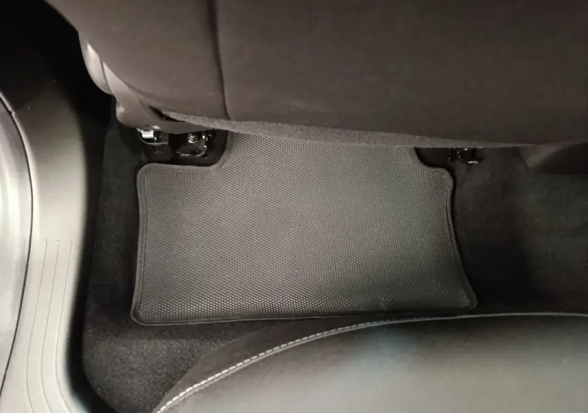 Vue intérieure du sol arrière côté droit de la Renault Clio gris clair, tapis de sol noir avec surpiqûres blanches visibles.