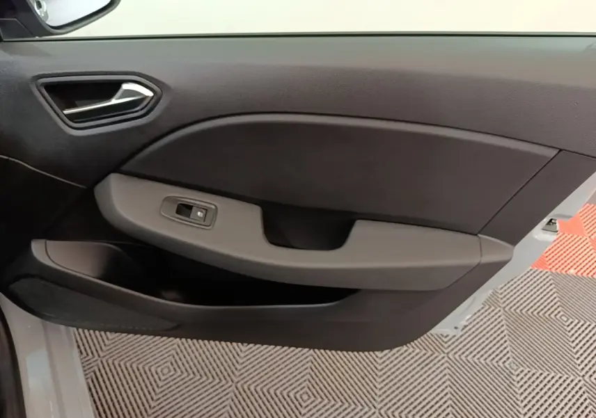 Vue intérieure côté gauche de la porte avant d’une Renault Clio gris clair, avec poignée et commande de vitre électrique.