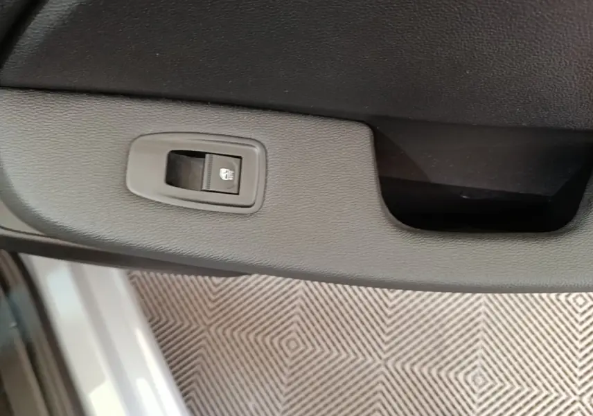 Gros plan sur le bouton de verrouillage de la porte intérieure d’une Renault Clio gris clair, vue côté conducteur.