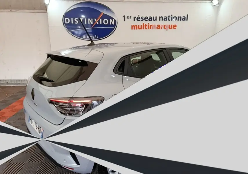 Vue 3/4 arrière d'une Renault Clio gris clair garée en intérieur, avec spoiler de toit et feux arrière LED visibles.