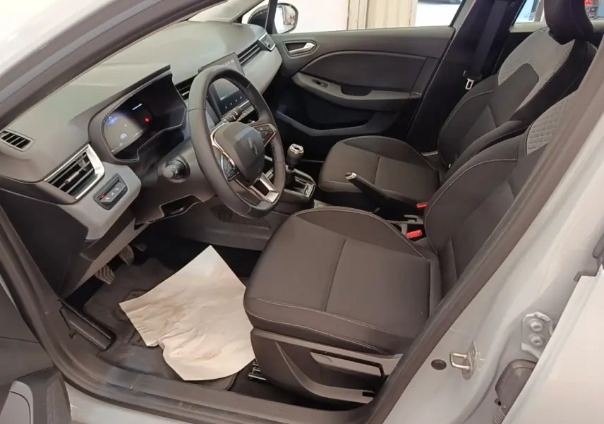 Vue intérieure côté conducteur de la Renault Clio gris clair 2025, volant cuir multifonctions et sièges tissu noirs.