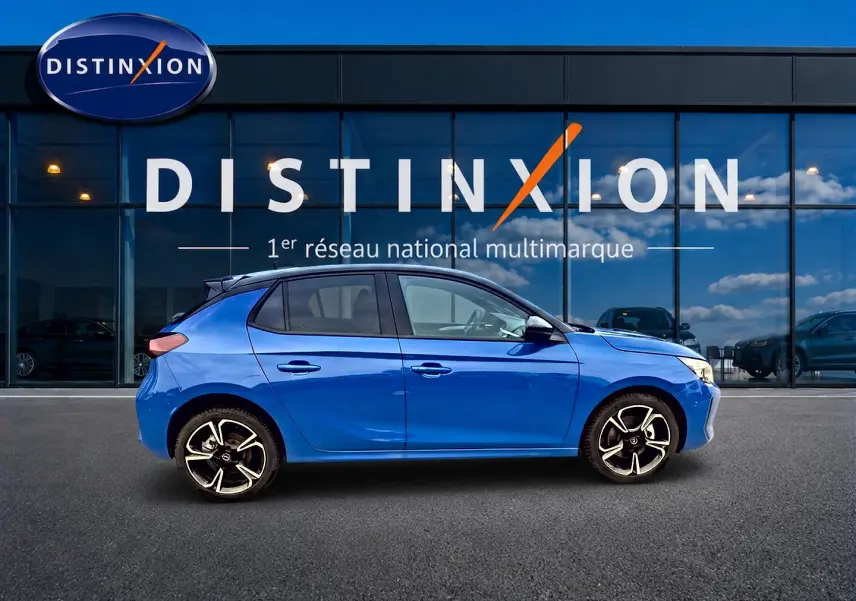 Profil côté gauche d'une Opel Corsa 1.2 turbo 100 gs bleu 2025 avec jantes alu et becquet arrière visible devant un showroom Distinxion.