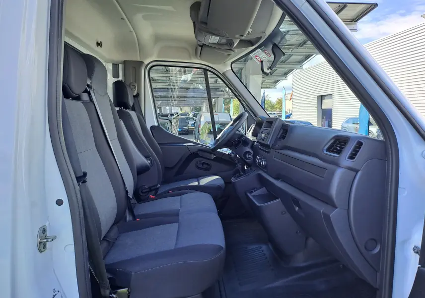 Vue intérieure côté conducteur du Nissan Interstar blanc 2024, montrant les sièges en tissu gris et le tableau de bord fonctionnel.