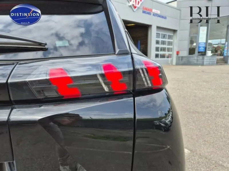 Gros plan sur le feu arrière droit rouge du Peugeot 2008 noir Perla Nera, avec reflet du ciel et bâtiment en arrière-plan.
