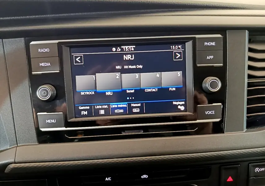 Écran tactile central du tableau de bord du Volkswagen Transporter blanc, affichant la radio NRJ en FM.