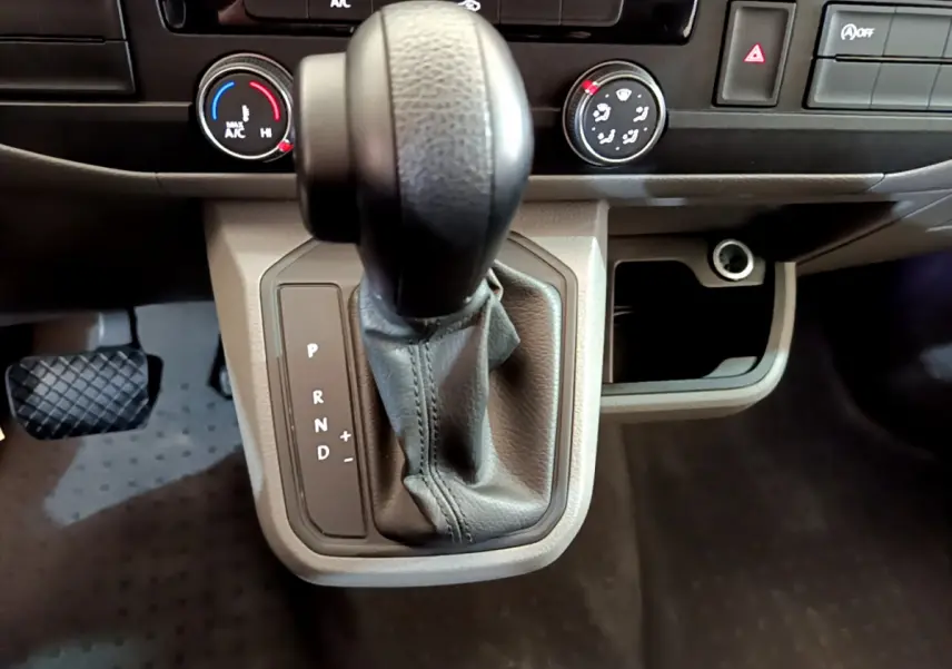 Le levier de vitesses automatique noir du Volkswagen Transporter 2.0 TDi 150 DSG7 avec commandes de climatisation en arrière-plan.