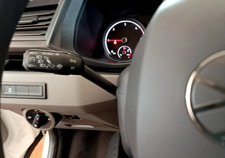 Vue partielle du tableau de bord et volant noir du Volkswagen Transporter blanc, avec compte-tours et commandes visibles.