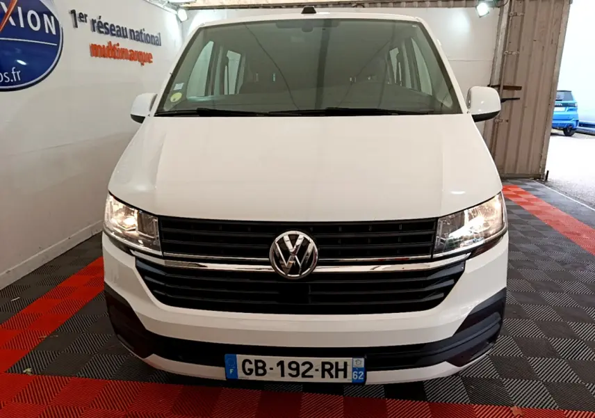 Vue frontale d'un Volkswagen Transporter blanc 2021 avec calandre noire et phares allumés dans un garage.