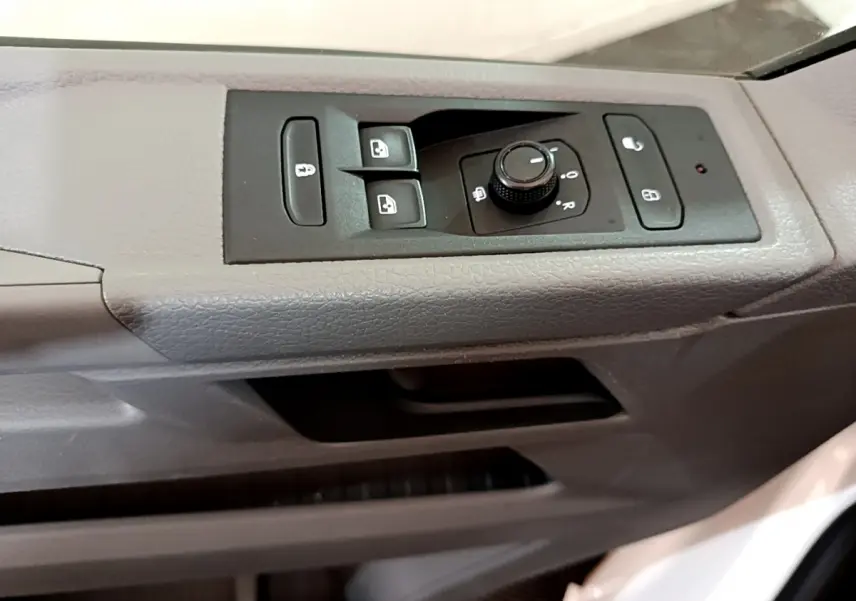 Gros plan sur les commandes de lève-vitres et réglage des rétroviseurs côté conducteur du Volkswagen Transporter blanc 2021.