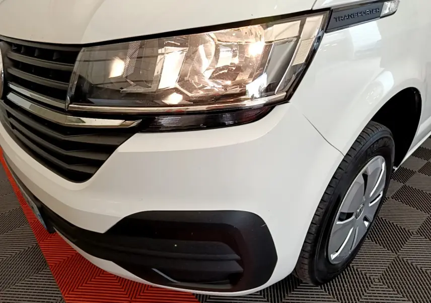 Gros plan sur l'avant droit blanc du Volkswagen Transporter 2.0 TDi 150 avec phare allumé et calandre noire.