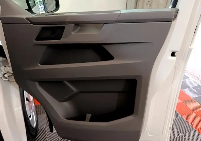 Vue rapprochée de la porte intérieure grise côté conducteur du Volkswagen Transporter blanc 2021, avec poignée intégrée.