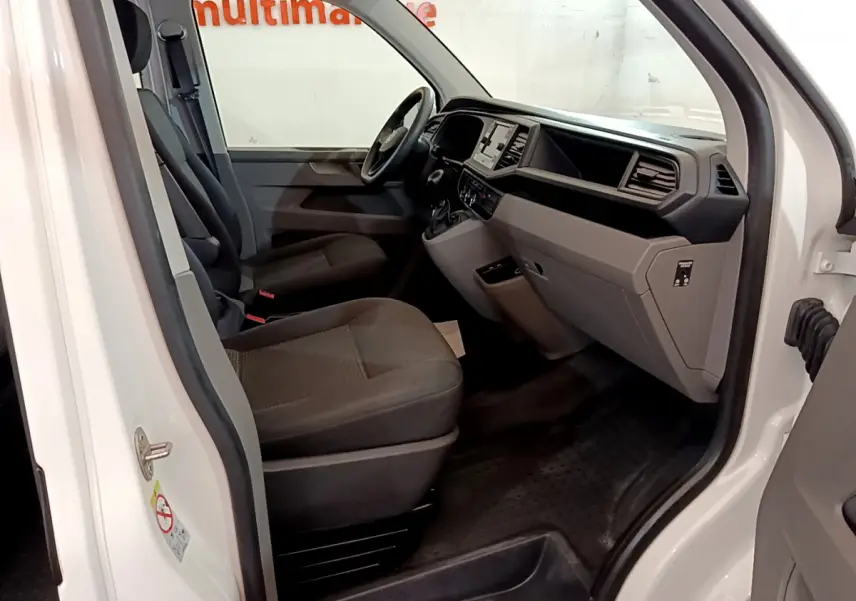 Intérieur côté conducteur du Volkswagen Transporter blanc 2021, montrant sièges et tableau de bord moderne.