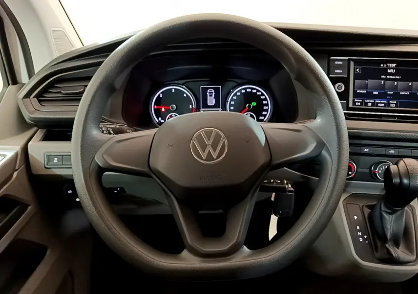Vue intérieure centrée sur le volant noir du Volkswagen Transporter 2.0 TDi 150 DSG7 avec tableau de bord et écran tactile.