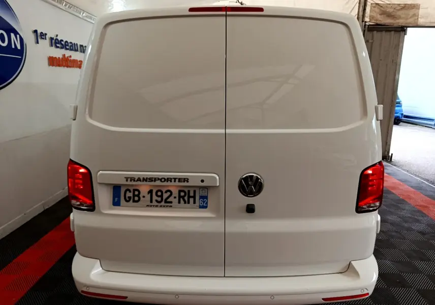 Vue arrière du Volkswagen Transporter blanc avec portes battantes fermées et feux rouges allumés dans un garage.