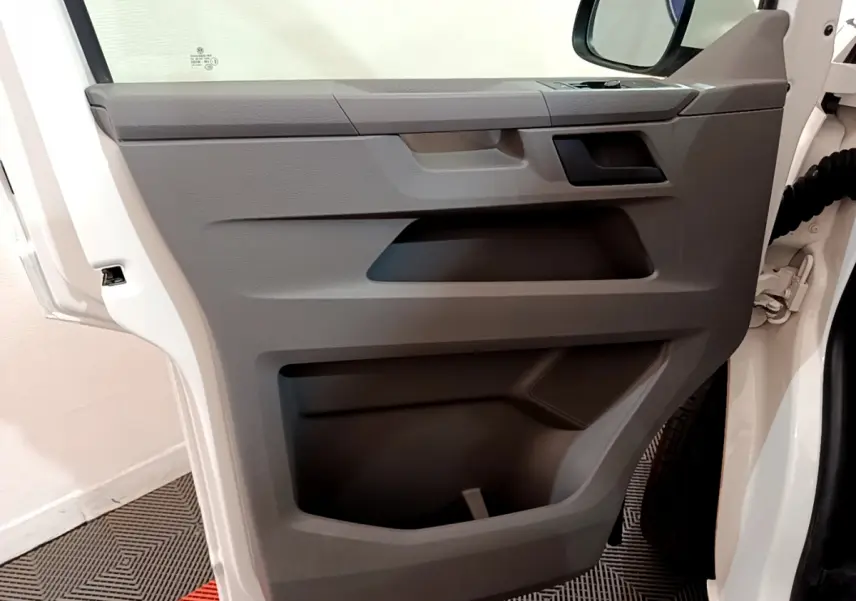 Vue rapprochée de la porte avant gauche blanche du Volkswagen Transporter 2.0 TDi 150 DSG7 Business avec rangement intégré.