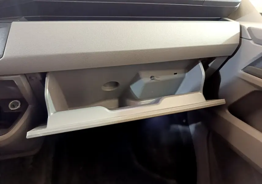 Vue rapprochée de la boîte à gants ouverte côté passager dans l'habitacle gris du Volkswagen Transporter blanc.