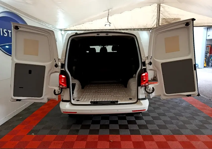 Vue arrière d'un Volkswagen Transporter blanc 2021 avec portes battantes ouvertes montrant l'espace de chargement vide.