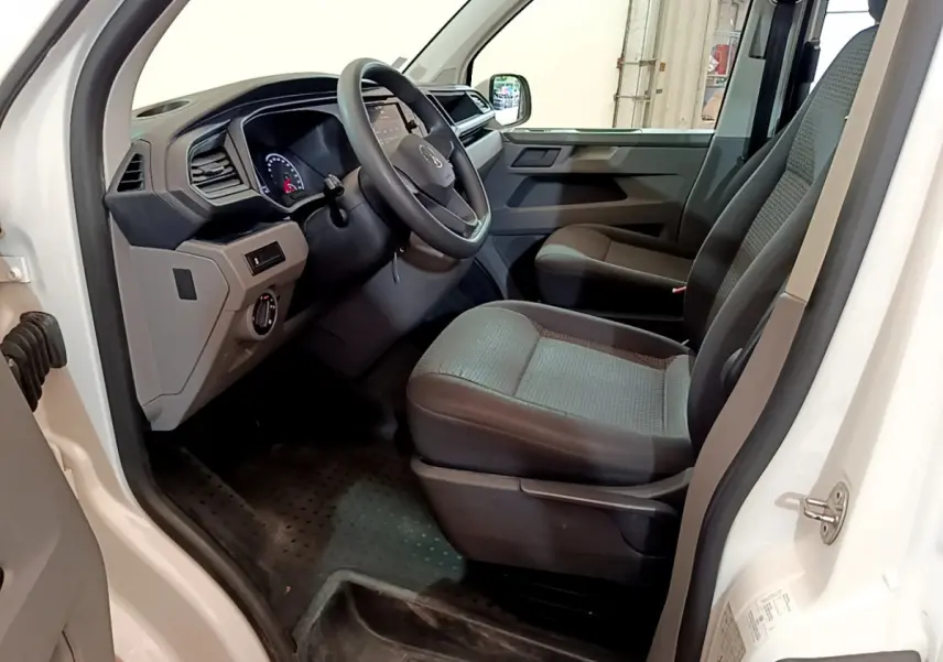 Intérieur côté conducteur du Volkswagen Transporter blanc, montrant le tableau de bord et les sièges avant gris foncé.