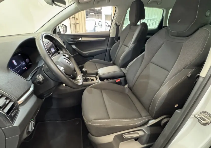 Intérieur vue côté conducteur du Skoda Karoq blanc 2024, sièges tissu noirs et volant cuir multifonctions.