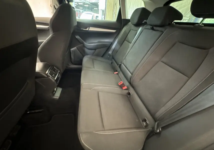 Vue intérieure côté droit des sièges arrière noirs du Skoda Karoq 2024 avec accoudoir central et ceintures visibles.