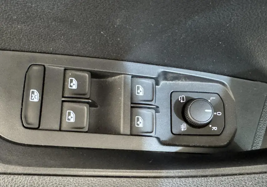 Gros plan sur les commandes de lève-vitres et réglage des rétroviseurs côté conducteur d’un Skoda Karoq blanc 2024.