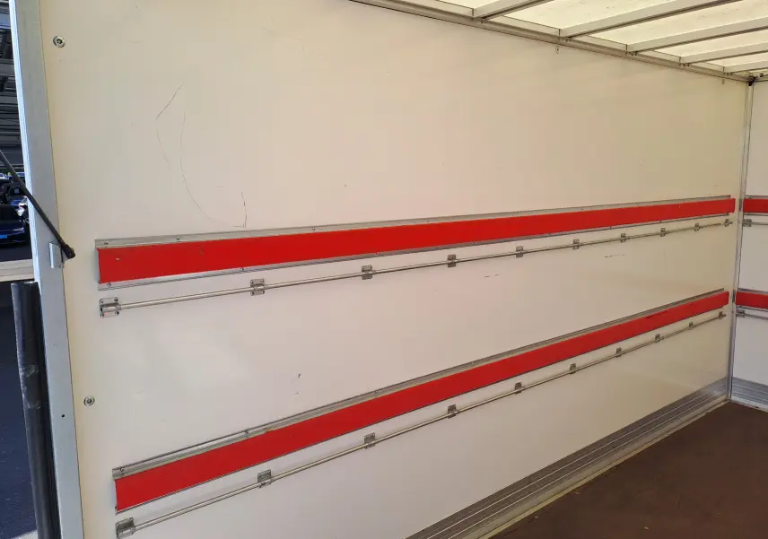 Vue intérieure du châssis cabine Nissan Interstar blanc 2024, montrant les parois avec rails métalliques et bandes rouges.