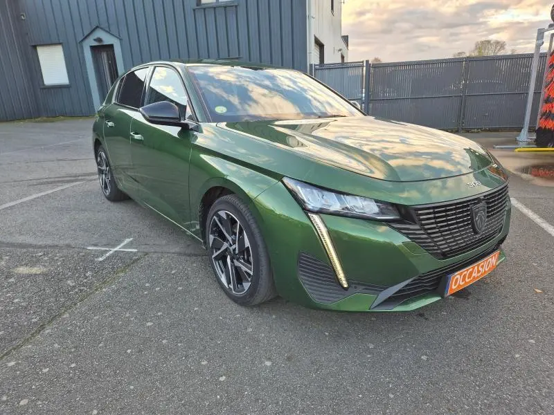 Peugeot 308 vert olivine vue 3/4 avant droit avec calandre noire et feux LED verticaux distinctifs.
