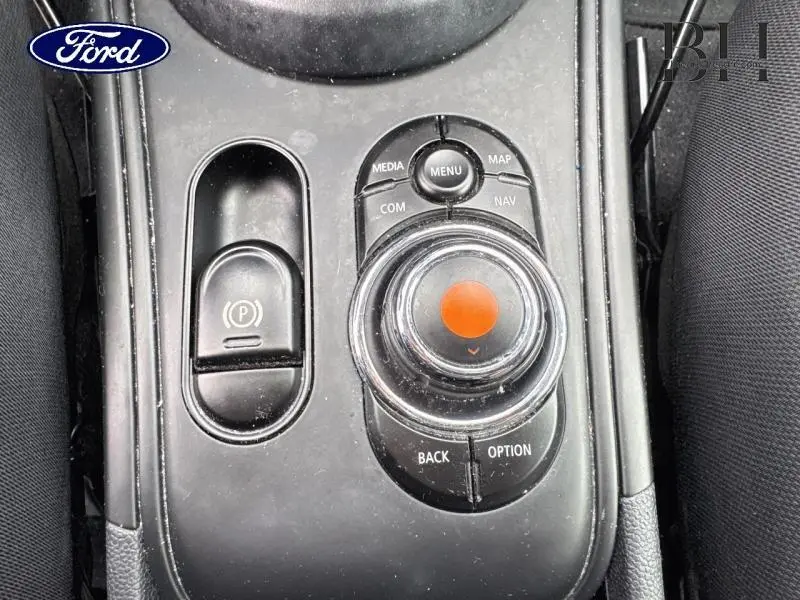 Gros plan sur la molette de commande centrale noire avec bouton orange du MINI Countryman Chili Red, entourée de boutons fonctionnels.