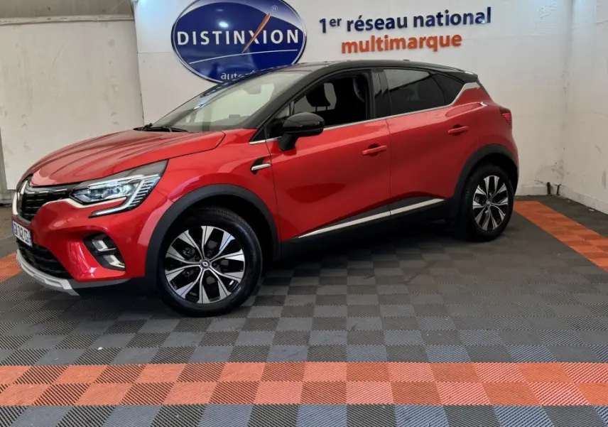 Renault Captur rouge en 3/4 avant droit, toit noir, jantes alliage et feux LED visibles en intérieur showroom.