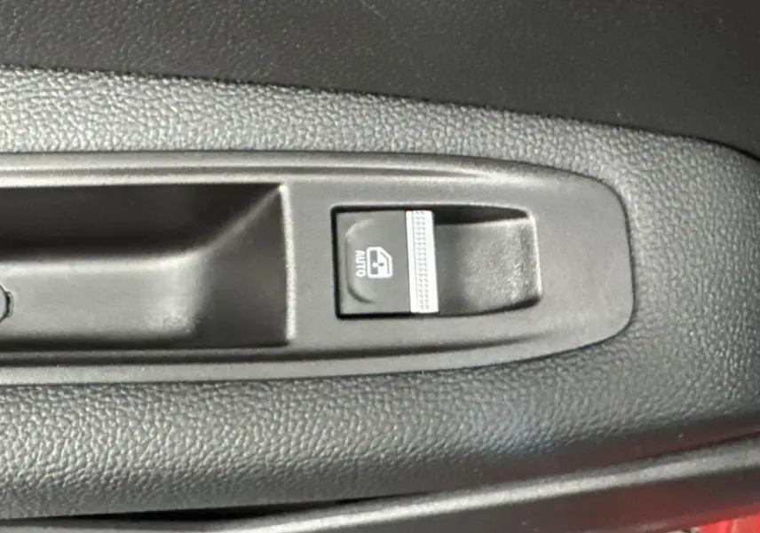 Gros plan sur le bouton de commande de la vitre électrique avant dans l'habitacle d'un Renault Captur rouge 2024.