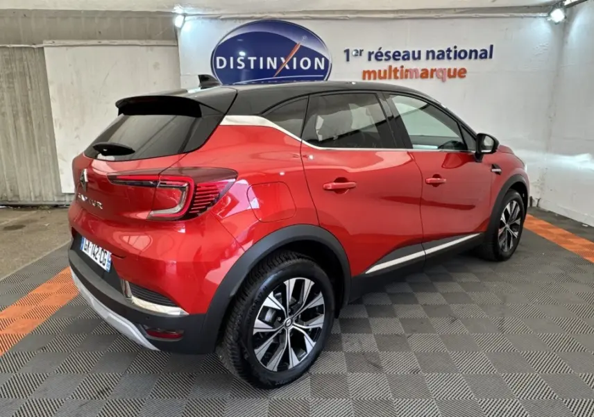 Vue 3/4 arrière droite d'un Renault Captur rouge 2024 avec toit noir et jantes alliage bicolores dans un garage.