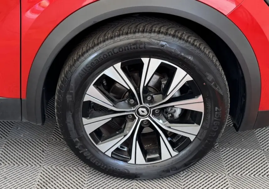 Gros plan sur la roue avant droite d’un Renault Captur rouge 2024 avec jante alliage bicolore et pneu toutes saisons.
