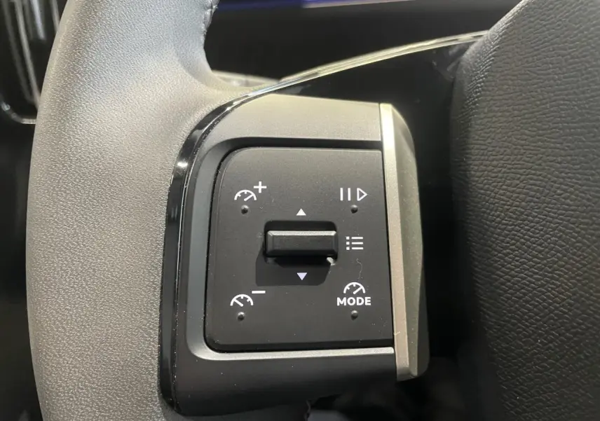 Gros plan sur les commandes de régulateur de vitesse au volant cuir noir de la Citroën C3 gris foncé.