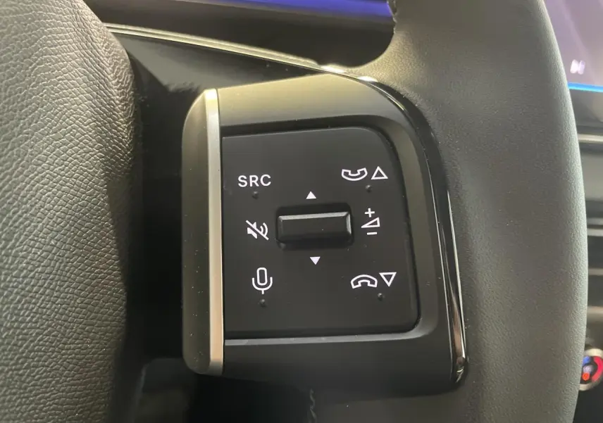 Gros plan sur les commandes multifonctions noires à gauche du volant gainé d'une Citroën C3 gris foncé 2025.