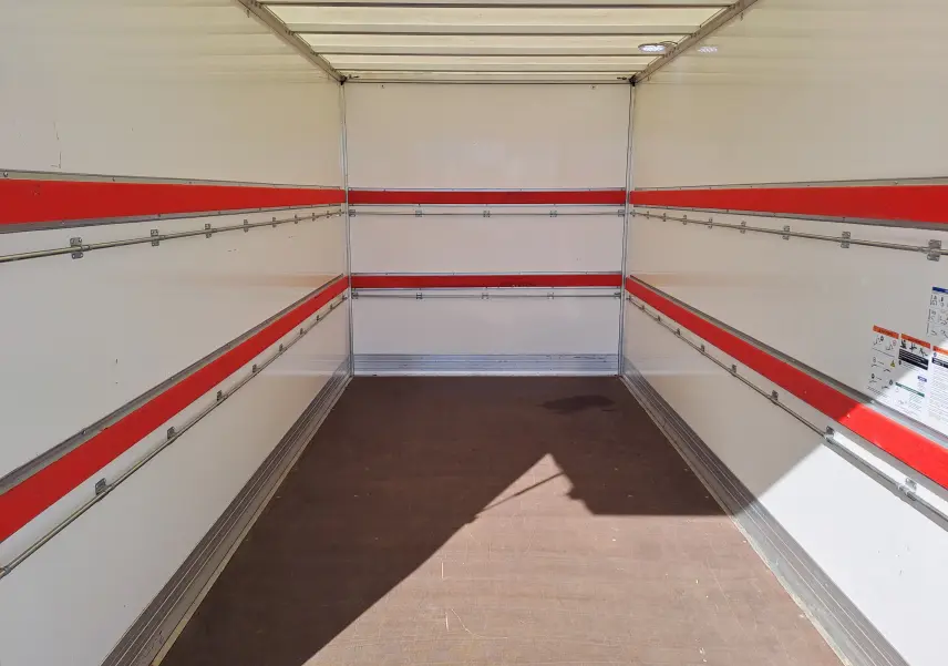 Intérieur vide du coffre d’un Nissan Interstar châssis cabine blanc, vue de l’arrière vers l’avant avec bandes rouges sur les parois.