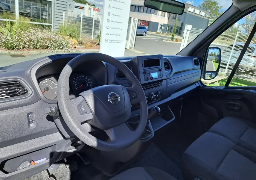 Vue intérieure côté conducteur du Nissan Interstar Châssis Cabine blanc 2024, tableau de bord simple avec volant et boîte manuelle.