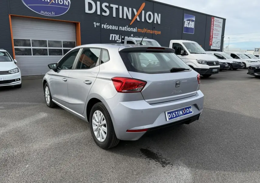 Vue 3/4 arrière droite d'une SEAT Ibiza 1.0 TSI argent Urban avec jantes alliage 15'' sur parking de concession.