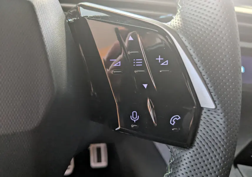 Gros plan sur les commandes tactiles noires du volant perforé côté gauche du Peugeot 3008 Hybrid 145 GT gris titane.