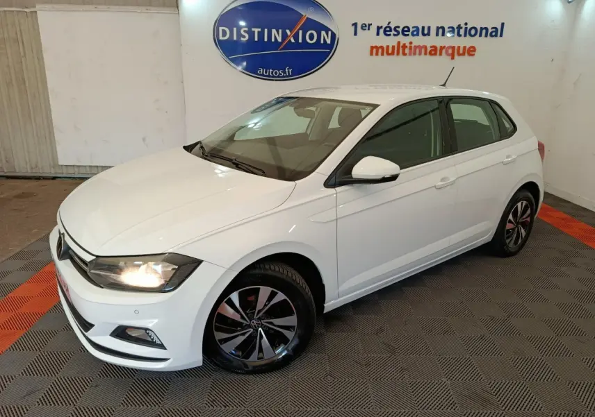 Volkswagen Polo blanc vue 3/4 avant droit en intérieur avec jantes alliage et phares allumés.