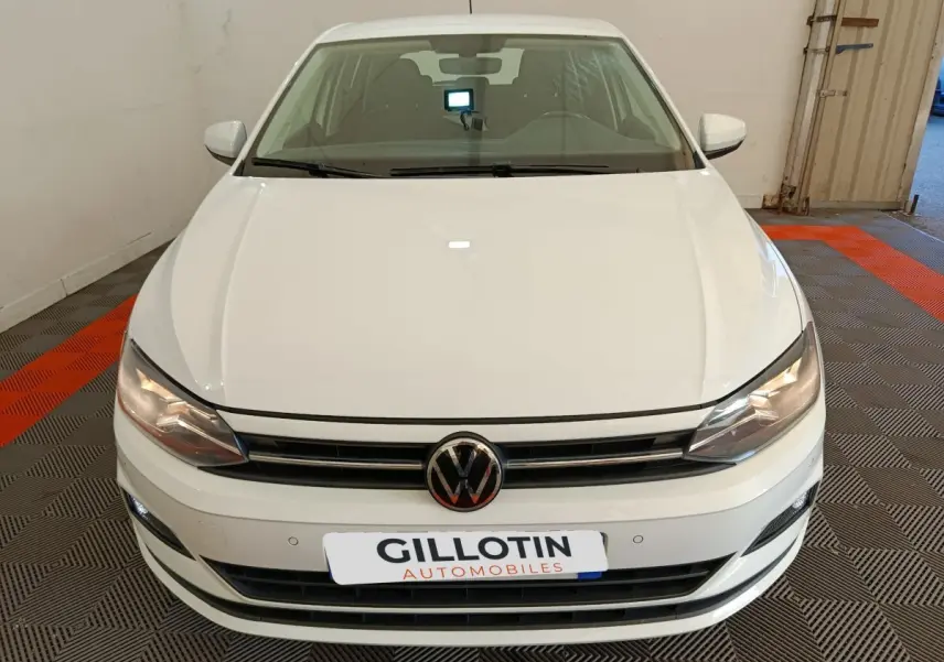 Vue avant d'une Volkswagen Polo blanche 2020, avec calandre noire et phares allumés dans un garage.