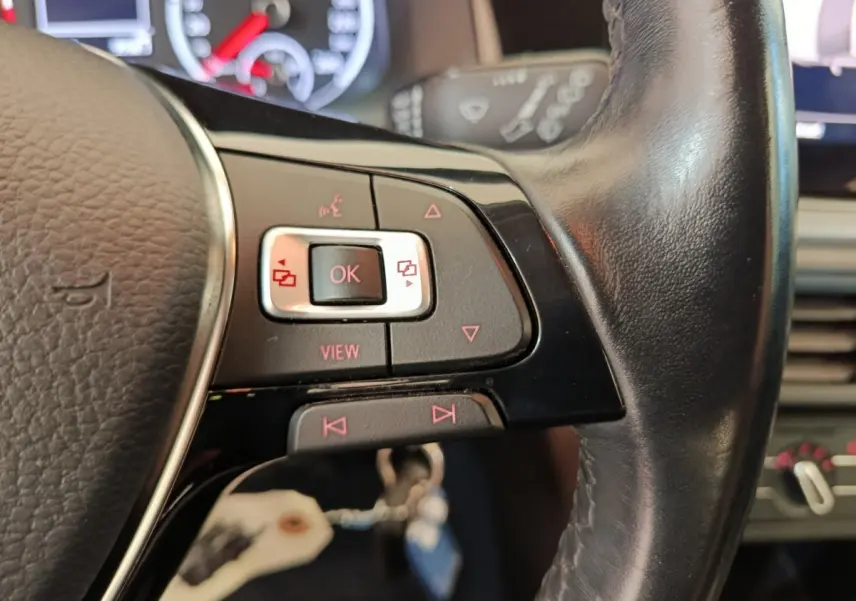 Gros plan sur les commandes gauche du volant cuir noir d'une Volkswagen Polo blanche, tableau de bord en arrière-plan flou.