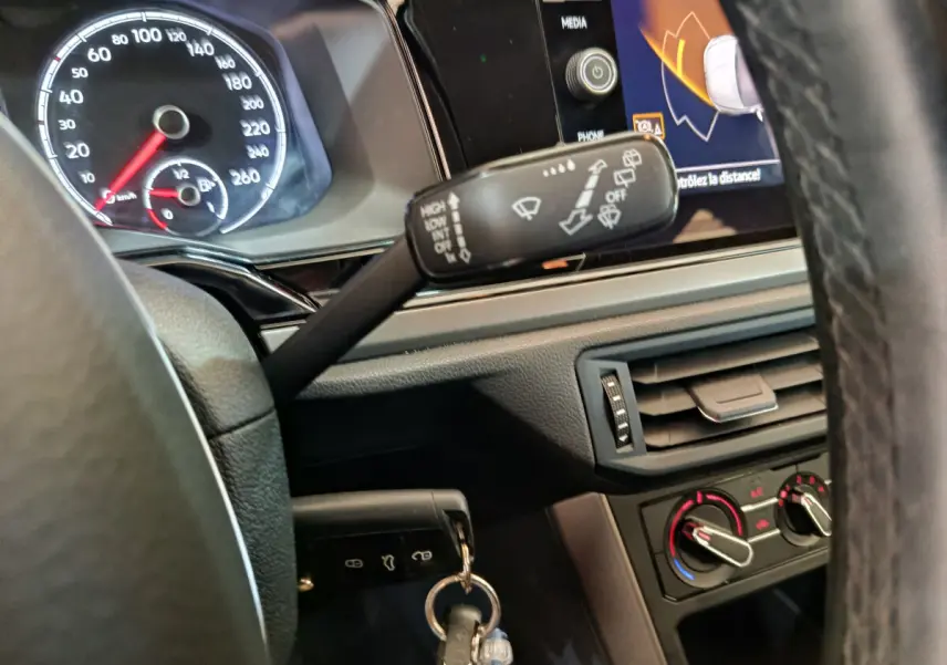 Gros plan sur le tableau de bord et volant de la Volkswagen Polo blanche 2020, avec écran tactile et commandes visibles.