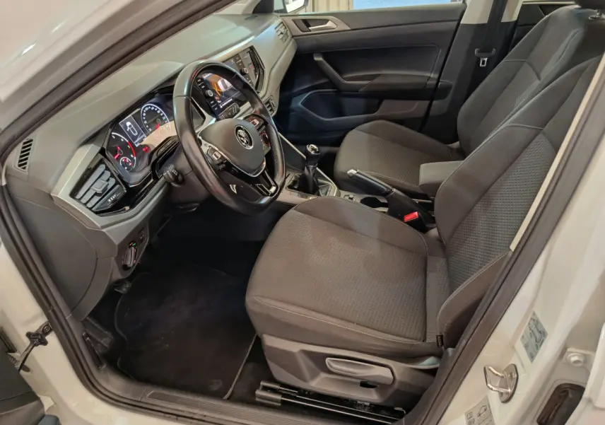 Intérieur avant droit de la Volkswagen Polo blanche 2020, montrant sièges tissu gris et tableau de bord avec écran tactile.