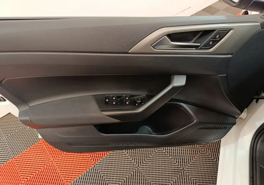 Vue rapprochée de la porte côté conducteur noire d'une Volkswagen Polo blanche, avec commandes électriques intégrées.