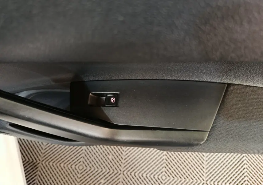 Gros plan sur le bouton de verrouillage des vitres sur la porte intérieure côté gauche d'une Volkswagen Polo blanche.